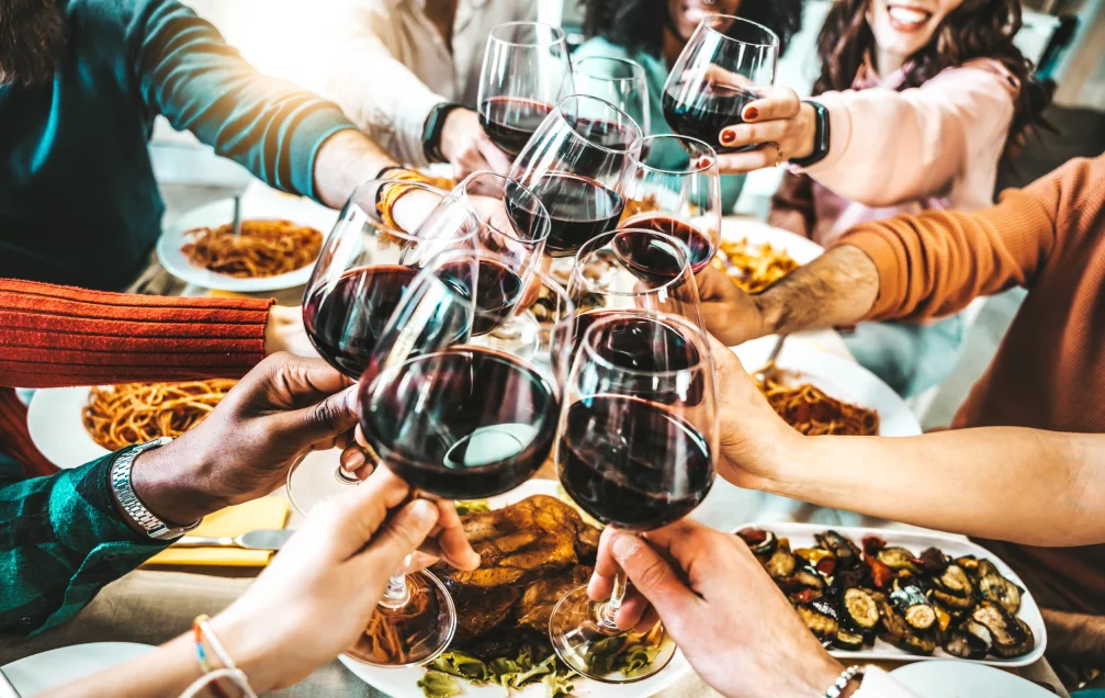 Group of friends raising glasses of red wine over plates of pasta and antipasti, enjoying Italian cuisine in Singapore at a celebratory dinner