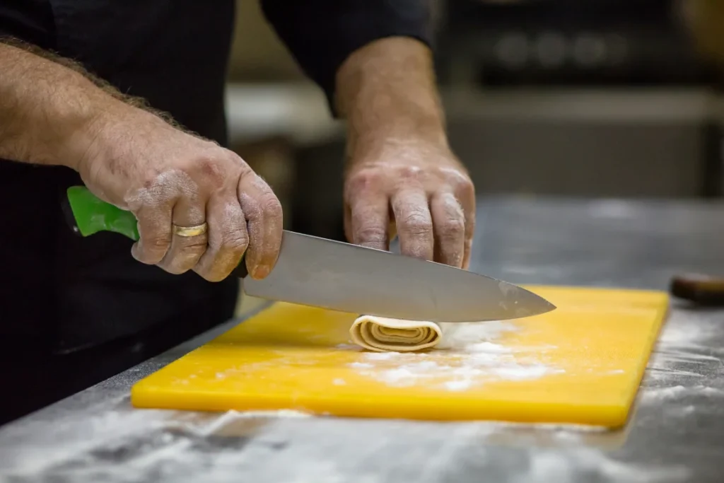  Chef slicing fresh handmade pasta dough in preparation for authentic Italian dishes, showcasing traditional craftsmanship at a leading pasta restaurant in Singapore.