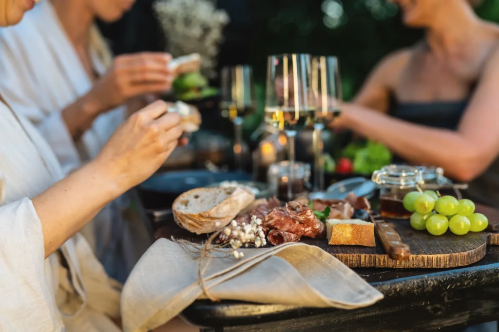 Friends sharing bread, wine, and charcuterie outdoors — a cosy evening of alfresco dining in Singapore.