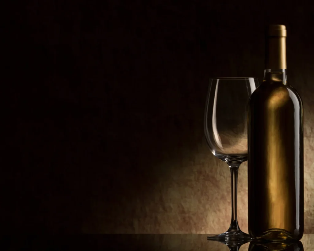 A golden wine bottle and empty glass set against a dark background, highlighting elegant liquor presentation and fine dining experiences in Singapore.