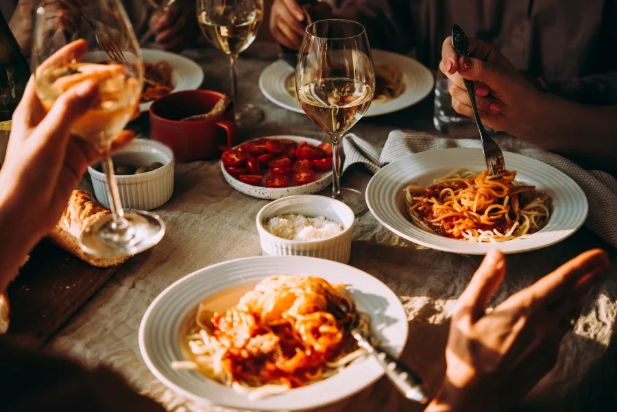 A warm dining scene with plates of pasta and glasses of wine shared among friends, representing the joy of pairing pasta with fine liquor in Singapore.